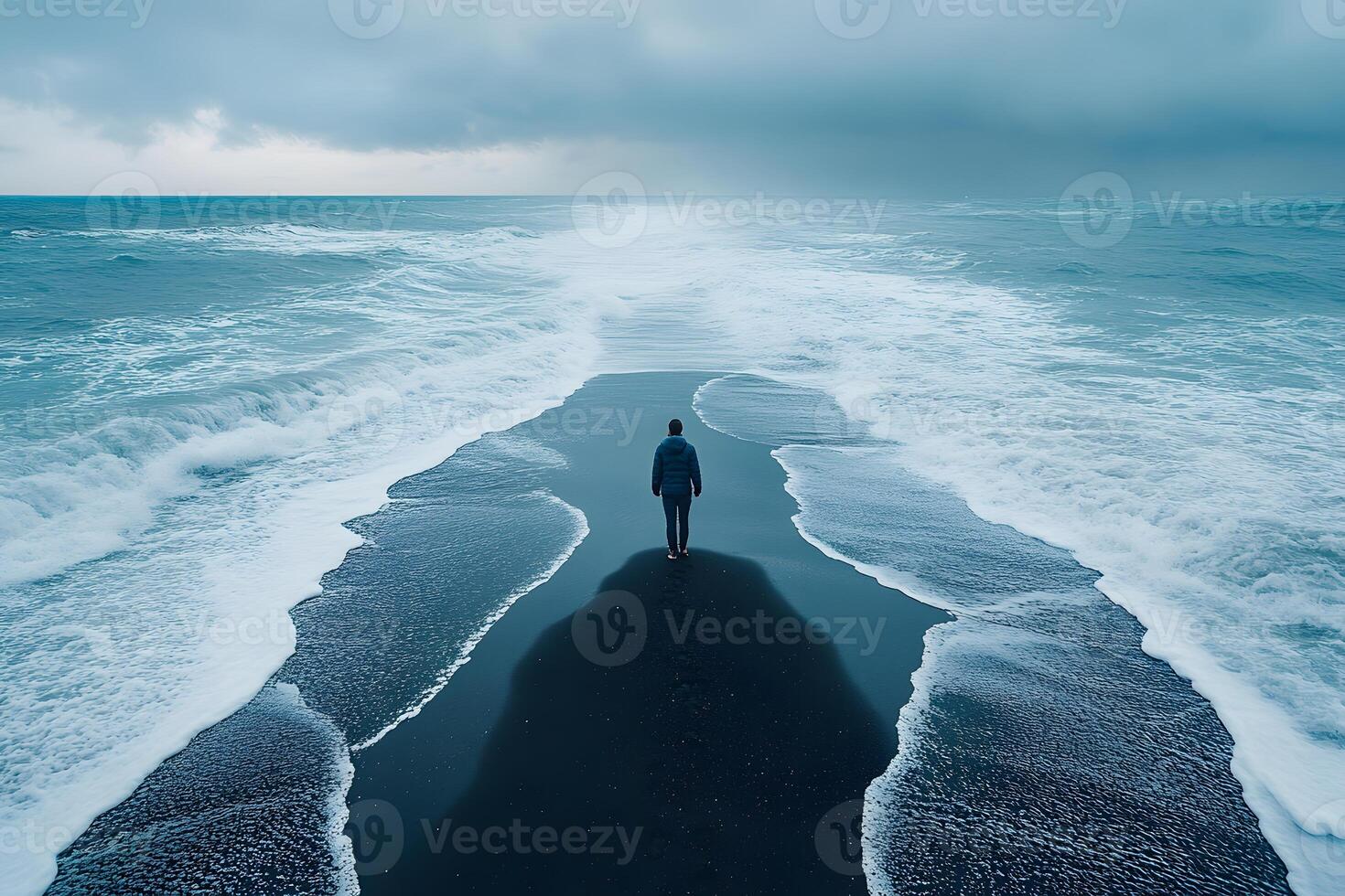 Solitary Walk on Dramatic Black Sand Beach Under Overcast Skies photo