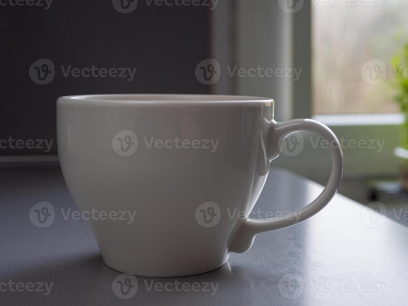 Large white mug brimming with steaming coffee rests on a table beside a window, basking in natural light and creating a warm, inviting atmosphere perfect for morning relaxation photo