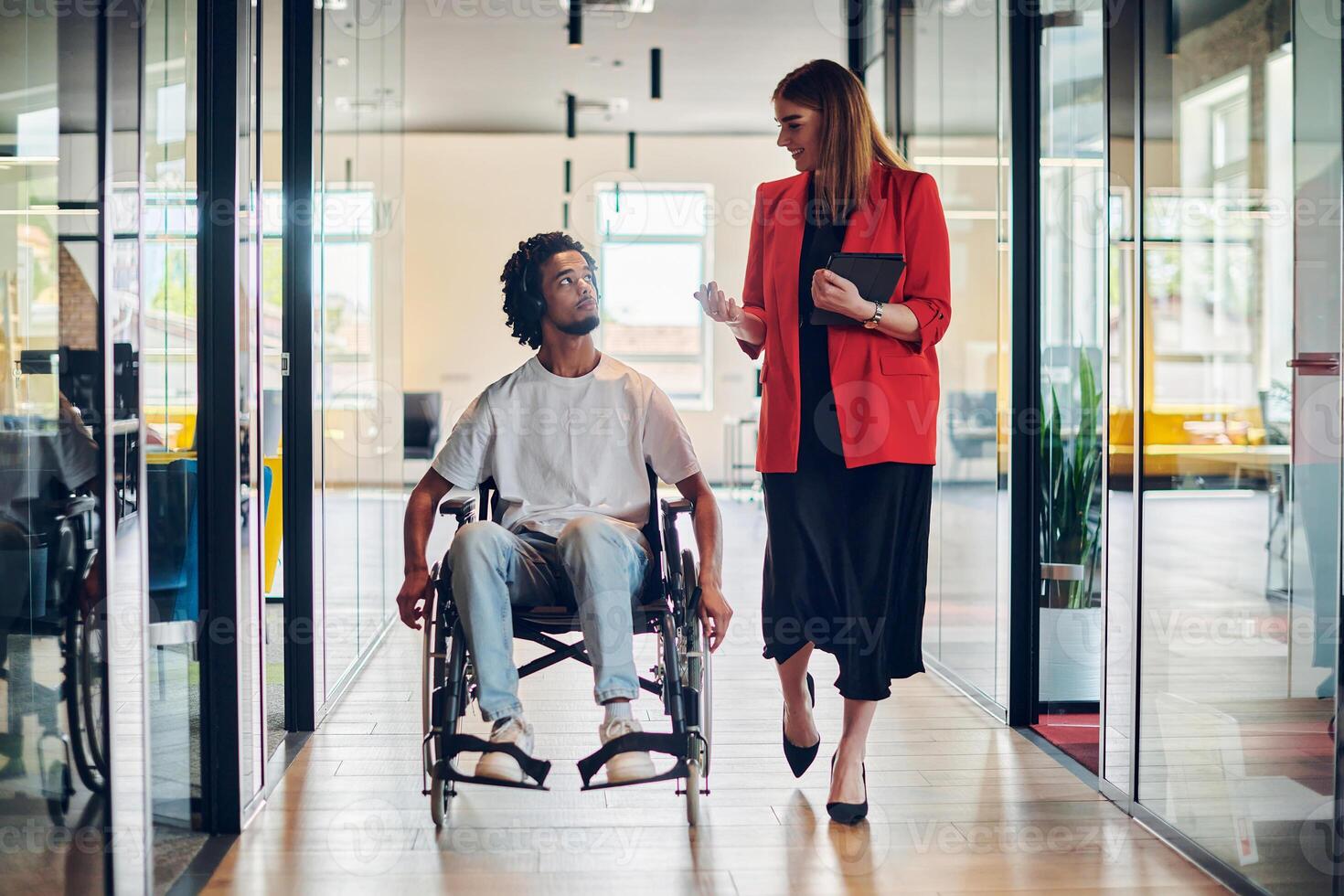 A group of young business people in a modern glass-walled office captures the essence of diversity and collaboration, while two colleagues, including an African American businessman in a wheelchair photo
