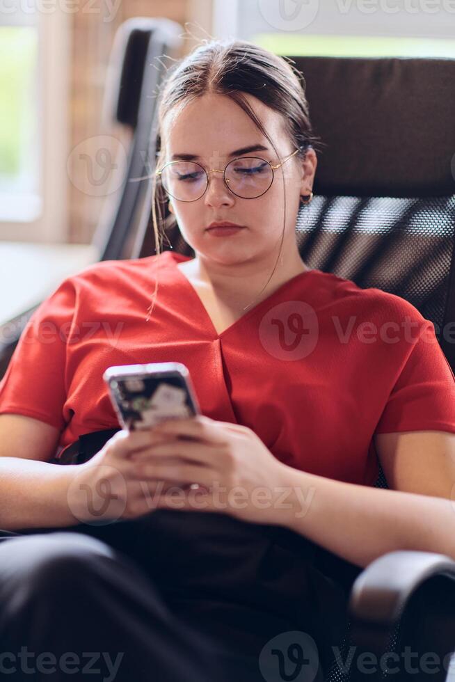 A businesswoman resting on a short break from work in a modern startup coworking center, using her smartphone to unwind and recharge. photo
