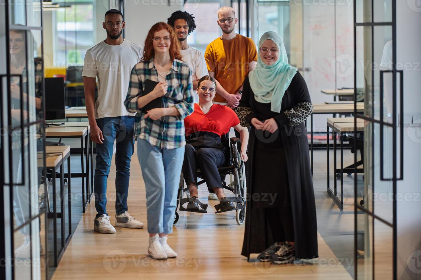 A diverse group of young business people congregates within a modern startup's glass-enclosed office, featuring inclusivity with a person in a wheelchair, an African American young man , and a hijab photo