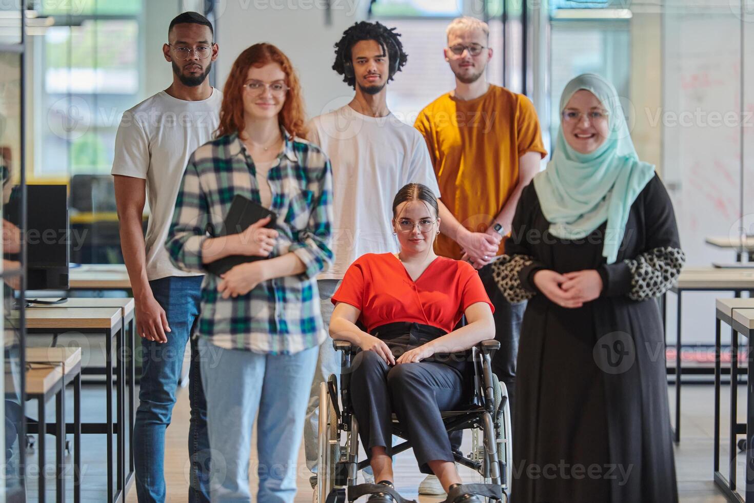 A diverse group of young business people congregates within a modern startup's glass-enclosed office, featuring inclusivity with a person in a wheelchair, an African American young man , and a hijab photo