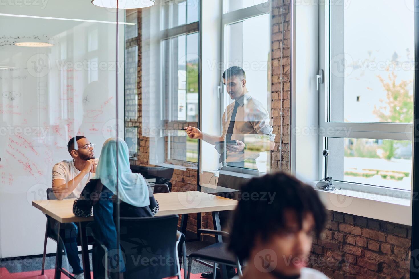 A business group, including an African American businessman in a wheelchair, collaborates within a modern glass office, actively engaged around a computer and laptop, collectively solving diverse photo