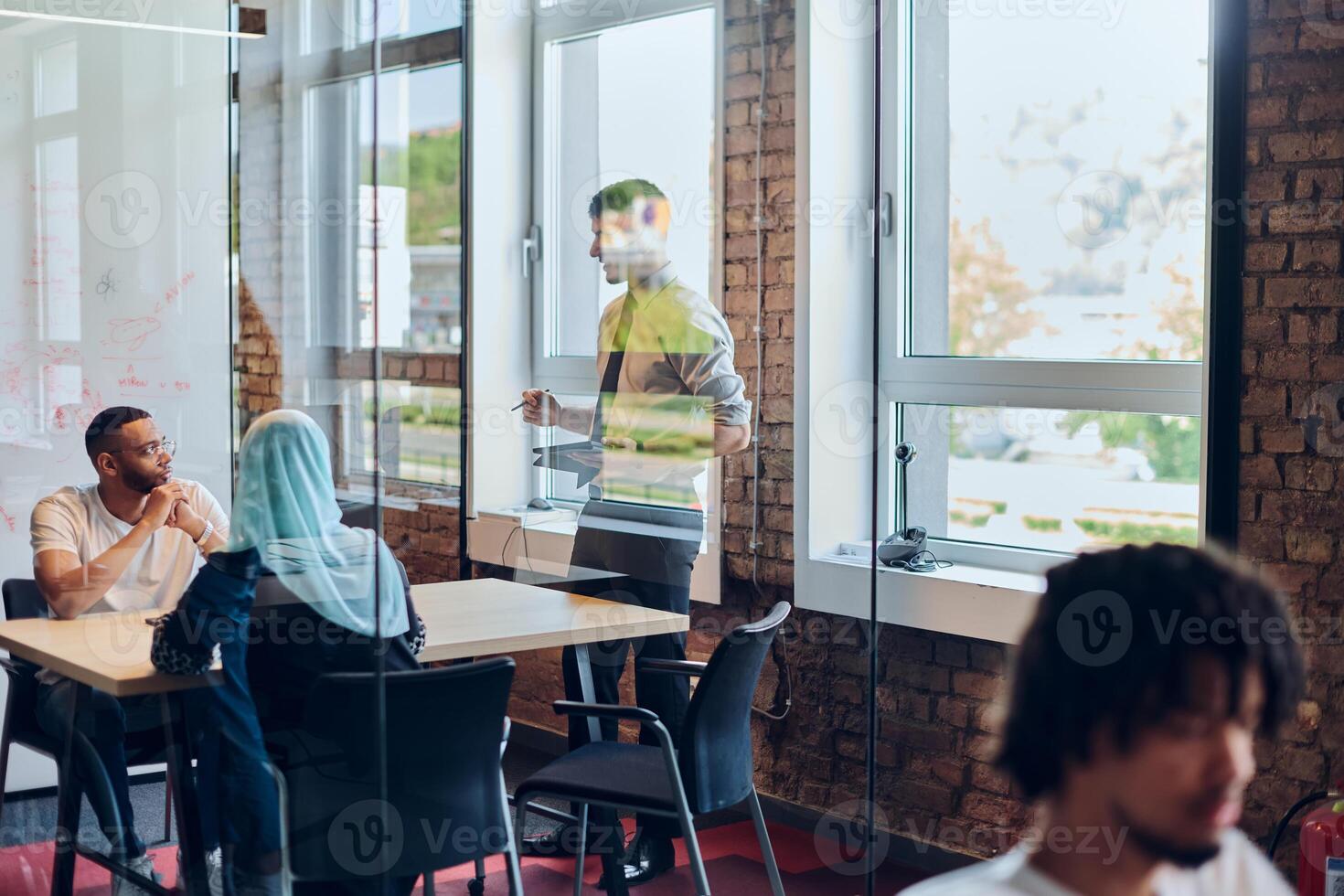 A business group, including an African American businessman in a wheelchair, collaborates within a modern glass office, actively engaged around a computer and laptop, collectively solving diverse photo