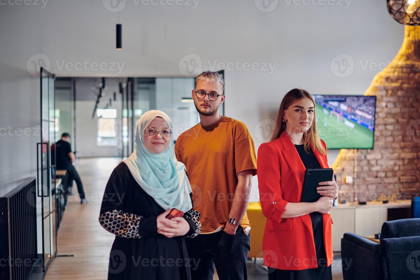 A group of young business colleagues, including a woman in a hijab, stands united in the modern corridor of a spacious startup coworking center, representing diversity and collaborative spirit. photo