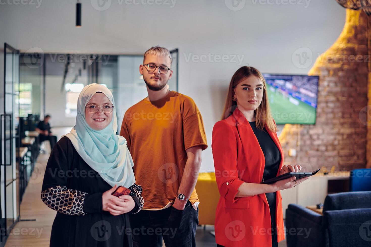 A group of young business colleagues, including a woman in a hijab, stands united in the modern corridor of a spacious startup coworking center, representing diversity and collaborative spirit. photo