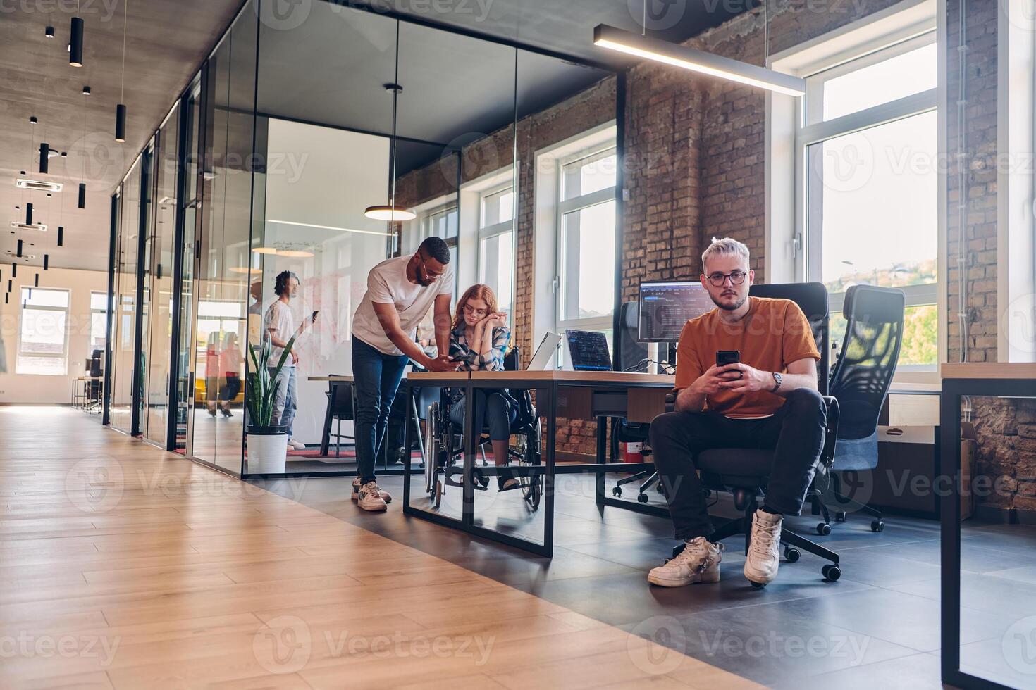 A diverse group of business professionals collaborates in a modern startup coworking center, utilizing a mix of paper-based and technological tools such as mobile phones and computers to collectively photo