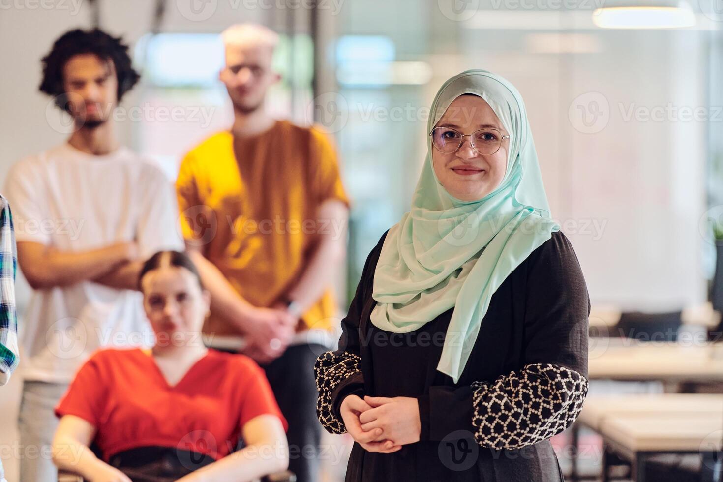 A diverse group of young business people congregates within a modern startup's glass-enclosed office, featuring inclusivity with a person in a wheelchair, an African American young man , and a hijab photo