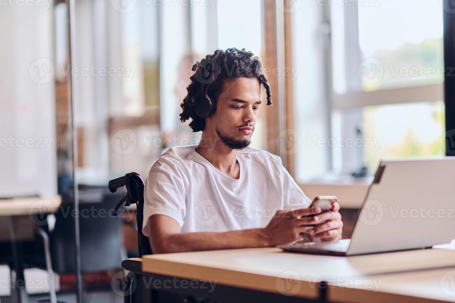 An African American businessman in a wheelchair takes a work break, using his smartphone while seated in a modern business startup coworking center, reflecting both inclusion and technology photo
