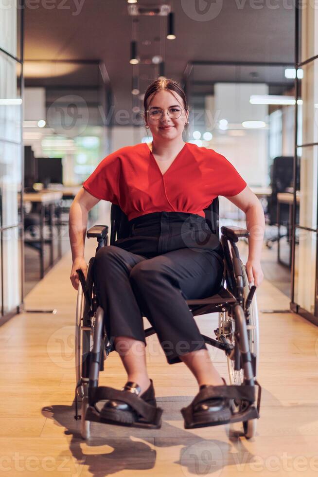 A modern young businesswoman in a wheelchair is surrounded by an inclusive workspace with glass-walled offices, embodying determination and innovation in the business world photo