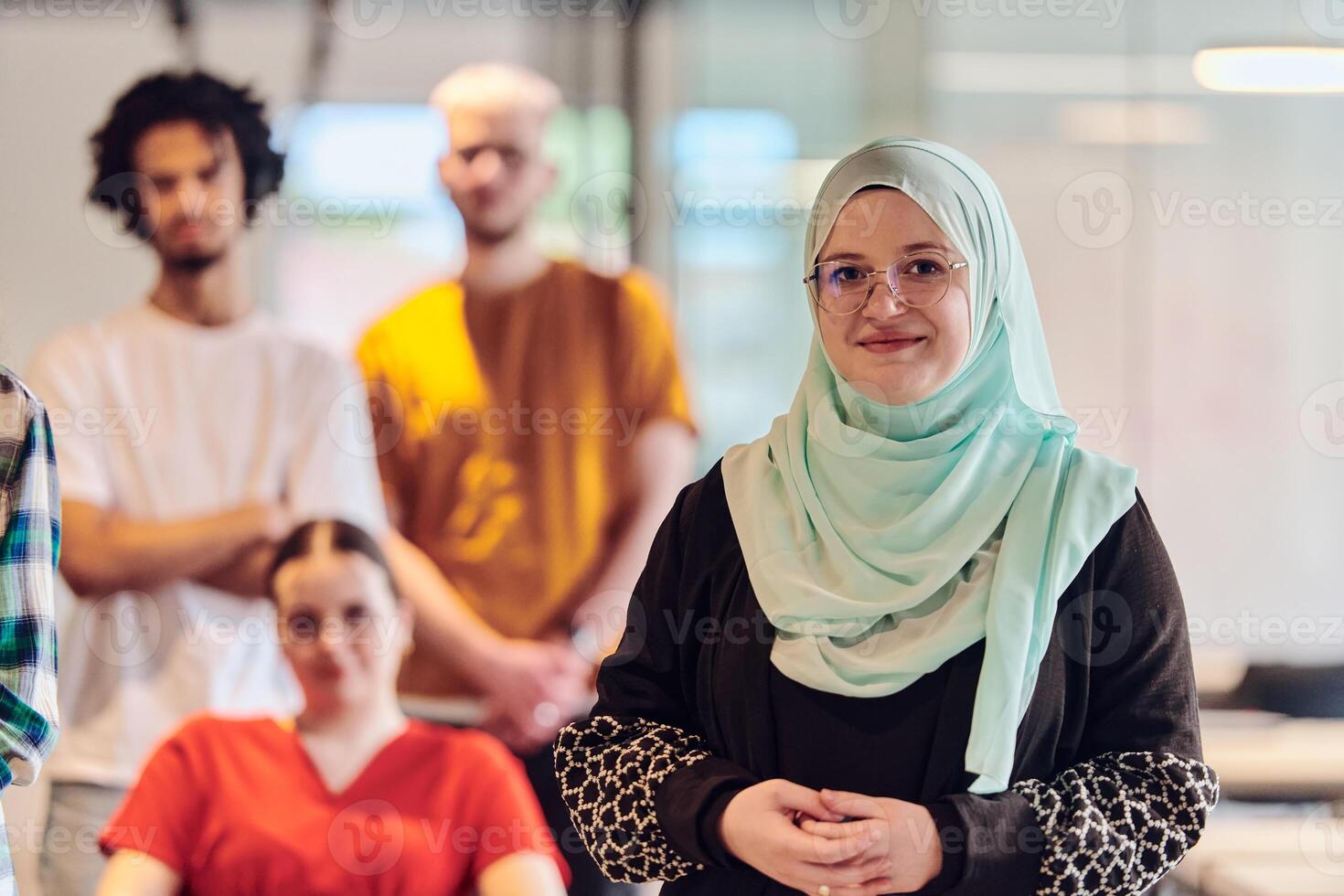 A diverse group of young business people congregates within a modern startup's glass-enclosed office, featuring inclusivity with a person in a wheelchair, an African American young man , and a hijab photo