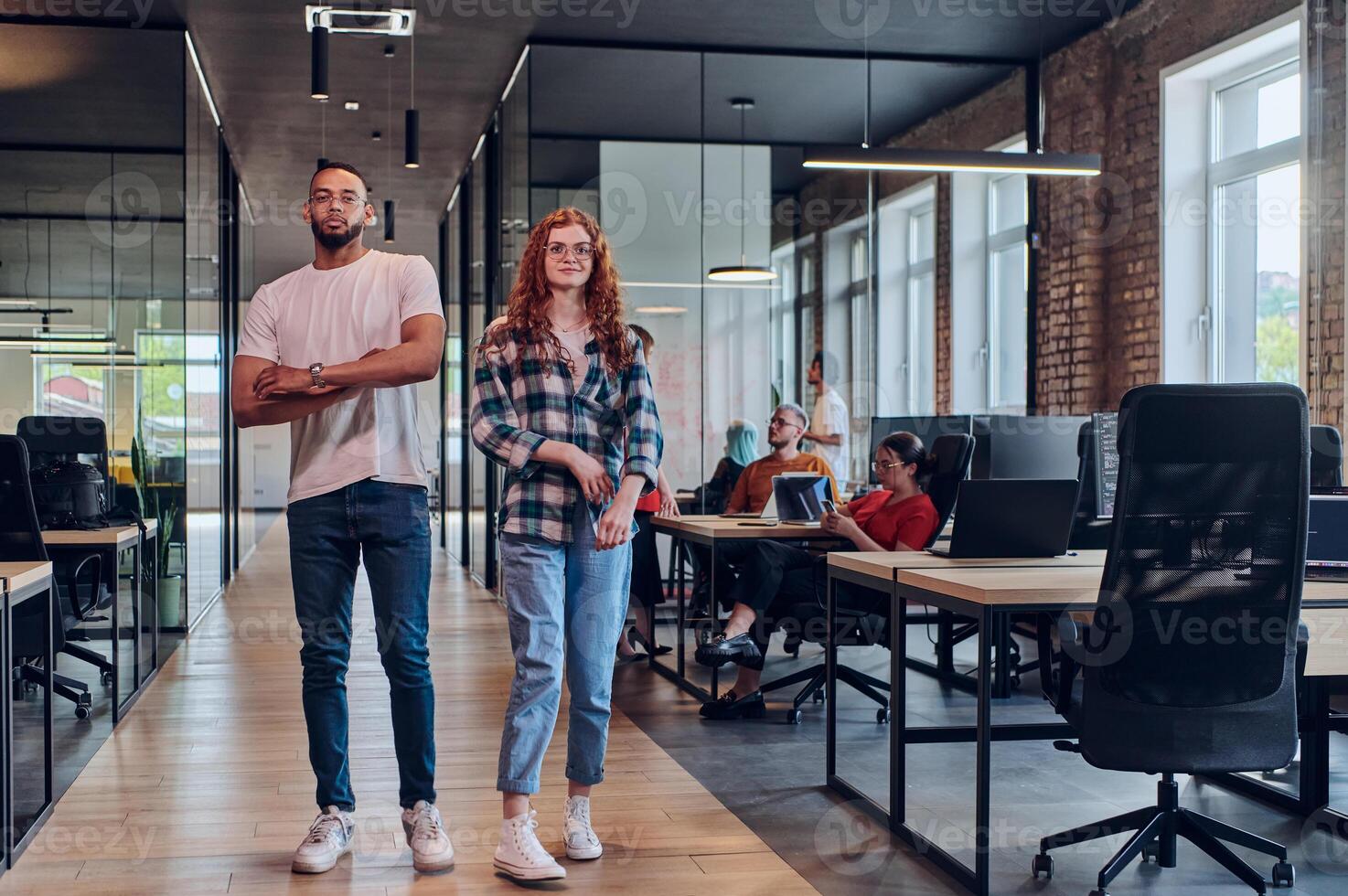 A young African American businessman and a modern businesswoman with orange hair stand side by side, arms crossed, exuding confidence and unity in a contemporary office setting, epitomizing dynamic photo