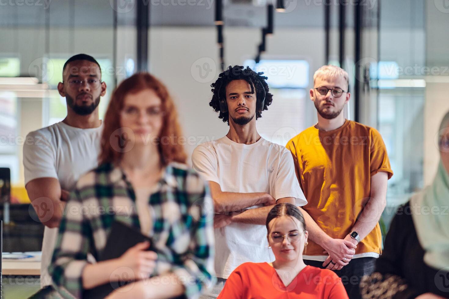 A diverse group of business people walking a corridor in the glass-enclosed office of a modern startup, including a person in a wheelchair and a woman wearing a hijab, showing a dynamic mix of photo