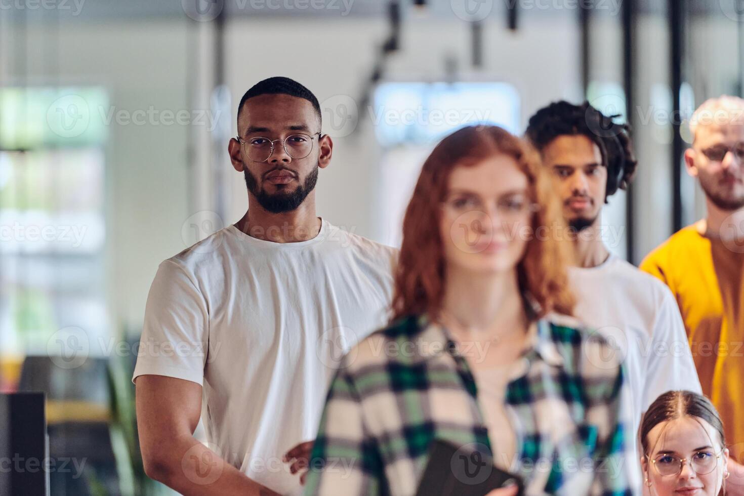 A diverse group of business people walking a corridor in the glass-enclosed office of a modern startup, including a person in a wheelchair and a woman wearing a hijab, showing a dynamic mix of photo