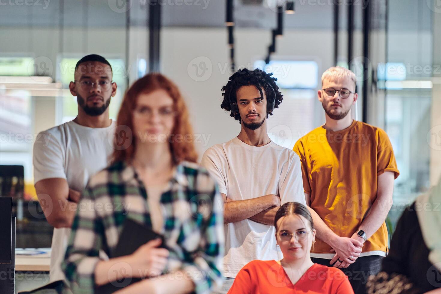 A diverse group of business people walking a corridor in the glass-enclosed office of a modern startup, including a person in a wheelchair and a woman wearing a hijab, showing a dynamic mix of photo