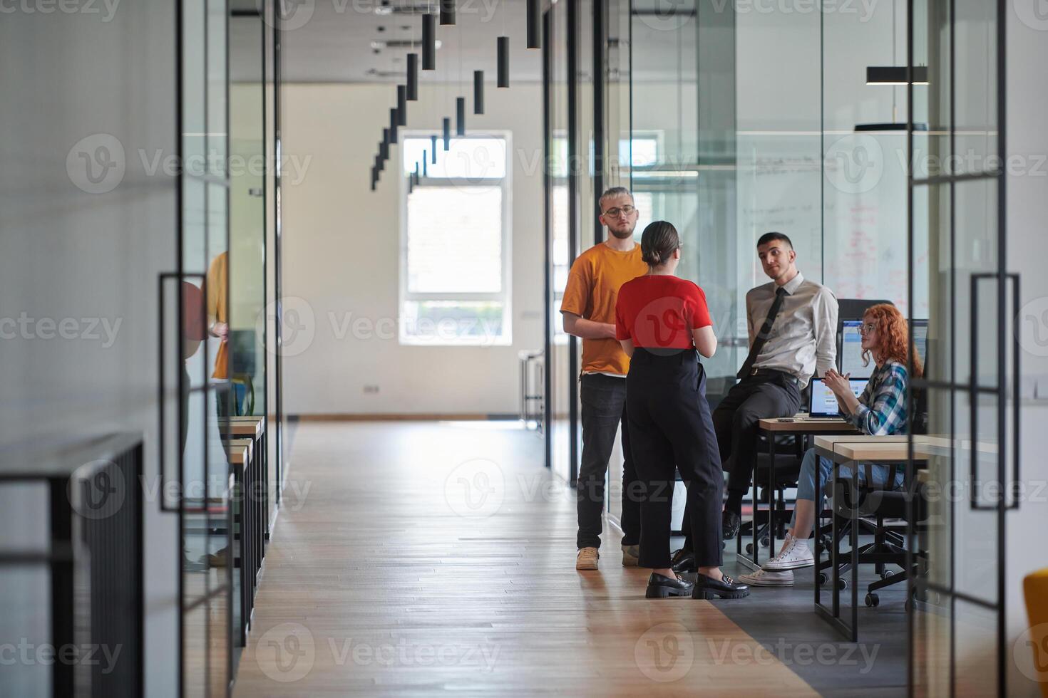 A business group, including an African American businessman in a wheelchair, collaborates within a modern glass office, actively engaged around a computer and laptop, collectively solving diverse photo
