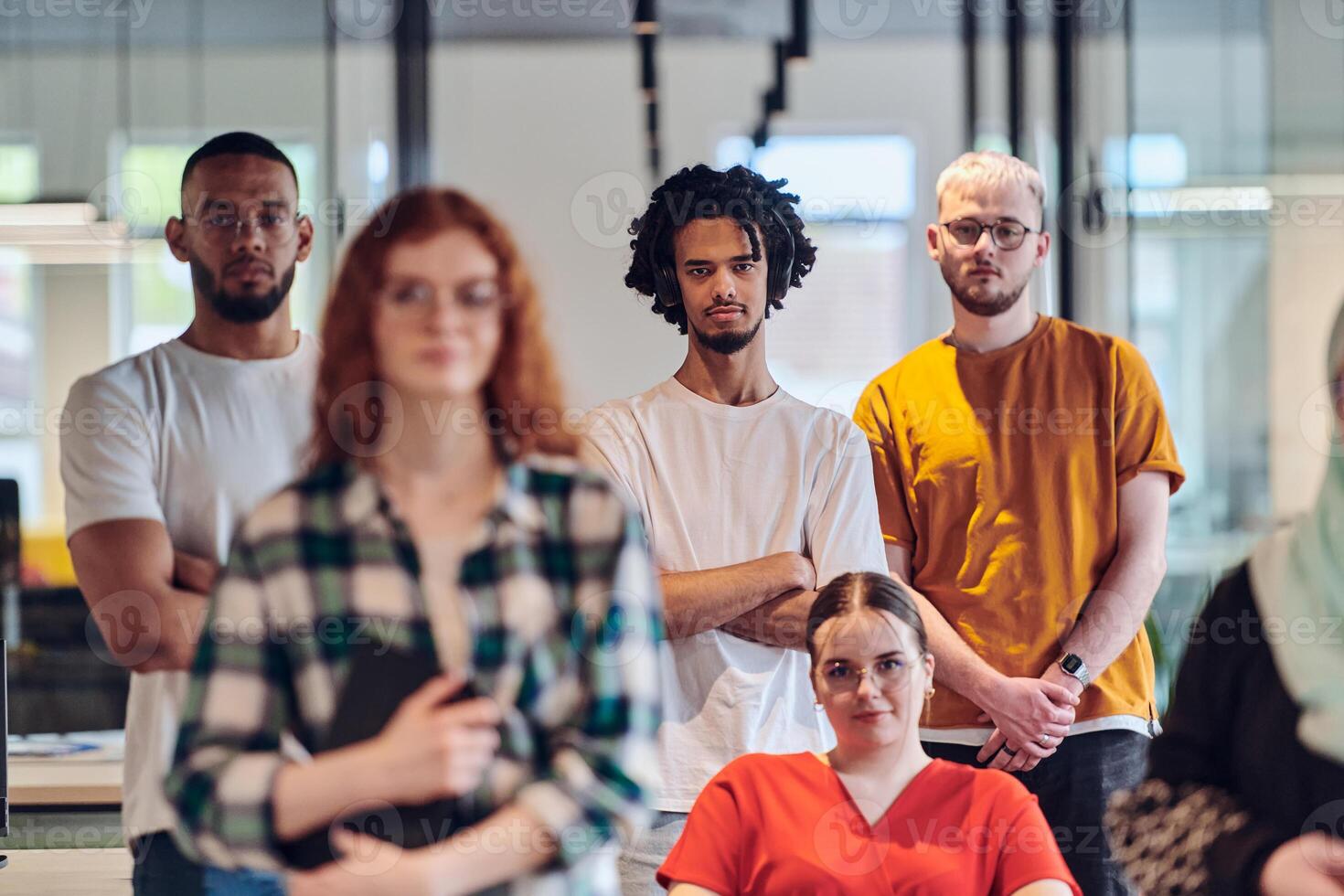 A diverse group of business people walking a corridor in the glass-enclosed office of a modern startup, including a person in a wheelchair and a woman wearing a hijab, showing a dynamic mix of photo