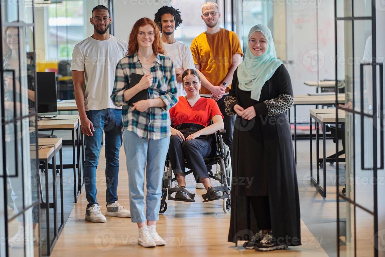 A diverse group of young business people congregates within a modern startup's glass-enclosed office, featuring inclusivity with a person in a wheelchair, an African American young man , and a hijab photo