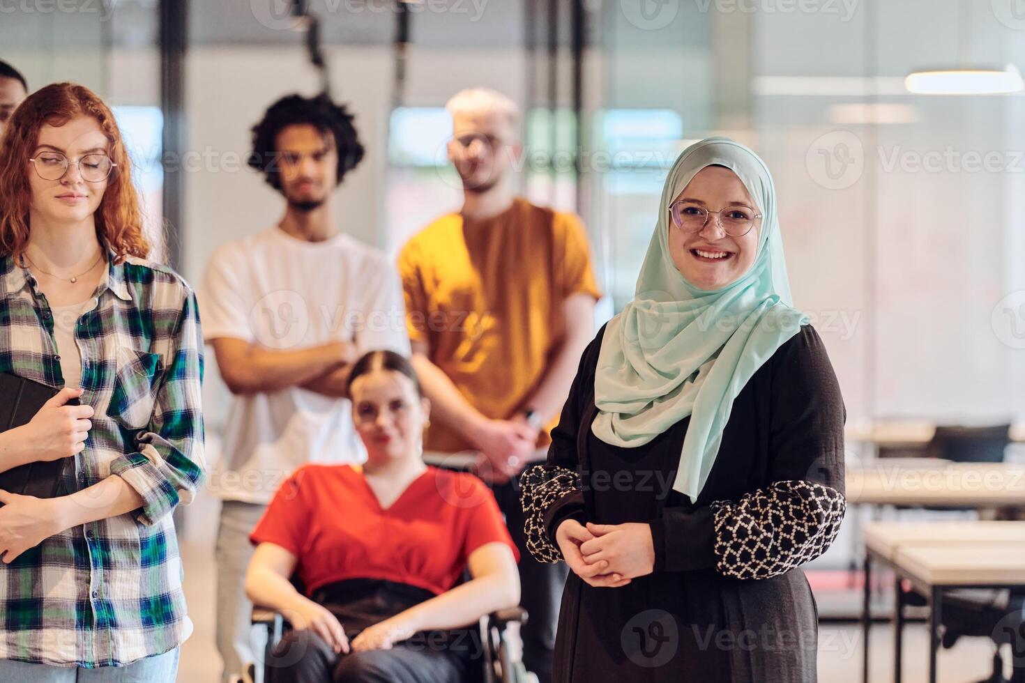 A diverse group of young business people congregates within a modern startup's glass-enclosed office, featuring inclusivity with a person in a wheelchair, an African American young man , and a hijab photo
