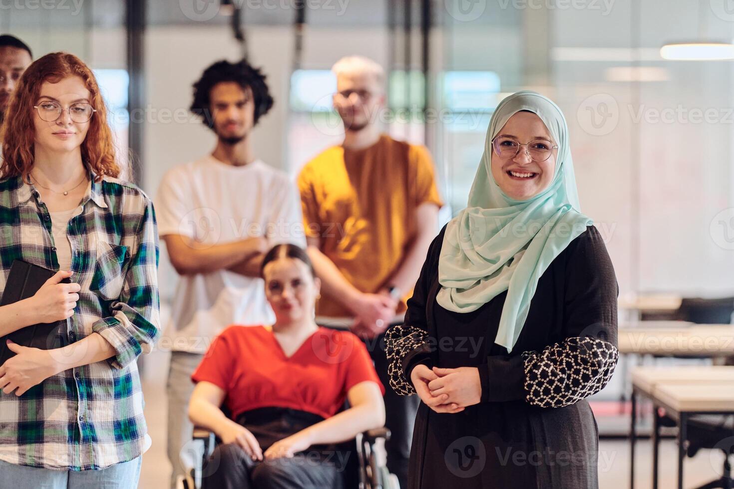 A diverse group of young business people congregates within a modern startup's glass-enclosed office, featuring inclusivity with a person in a wheelchair, an African American young man , and a hijab photo