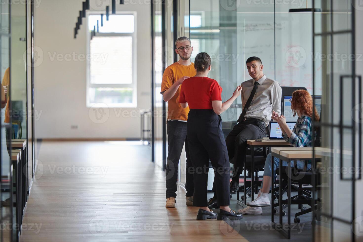 A business group, including an African American businessman in a wheelchair, collaborates within a modern glass office, actively engaged around a computer and laptop, collectively solving diverse photo