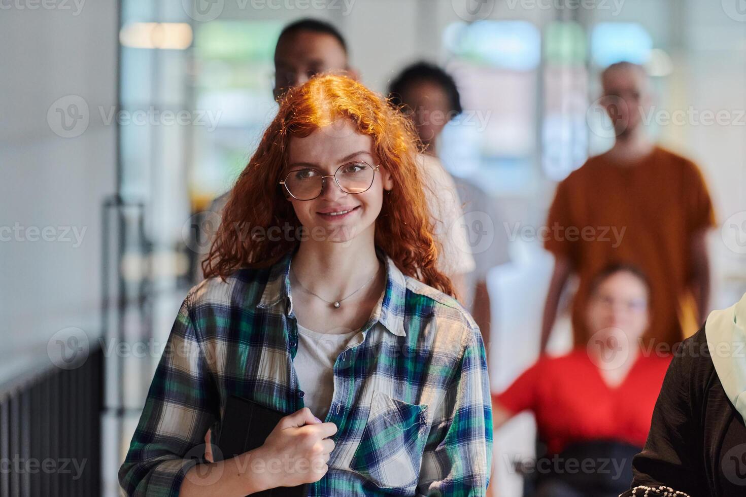 A diverse group of business people walking a corridor in the glass-enclosed office of a modern startup, including a person in a wheelchair and a woman wearing a hijab, showing a dynamic mix of photo