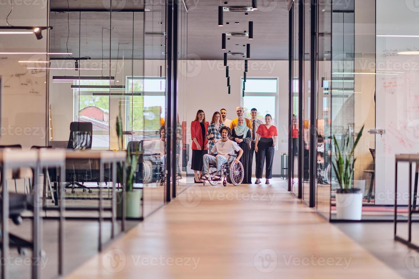 A diverse group of young business people congregates within a modern startup's glass-enclosed office, featuring inclusivity with a person in a wheelchair, an African American young man , and a hijab photo