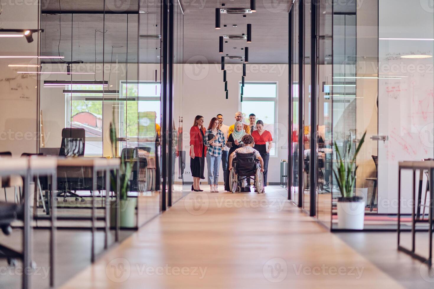 A diverse group of young business people congregates within a modern startup's glass-enclosed office, featuring inclusivity with a person in a wheelchair, an African American young man , and a hijab photo