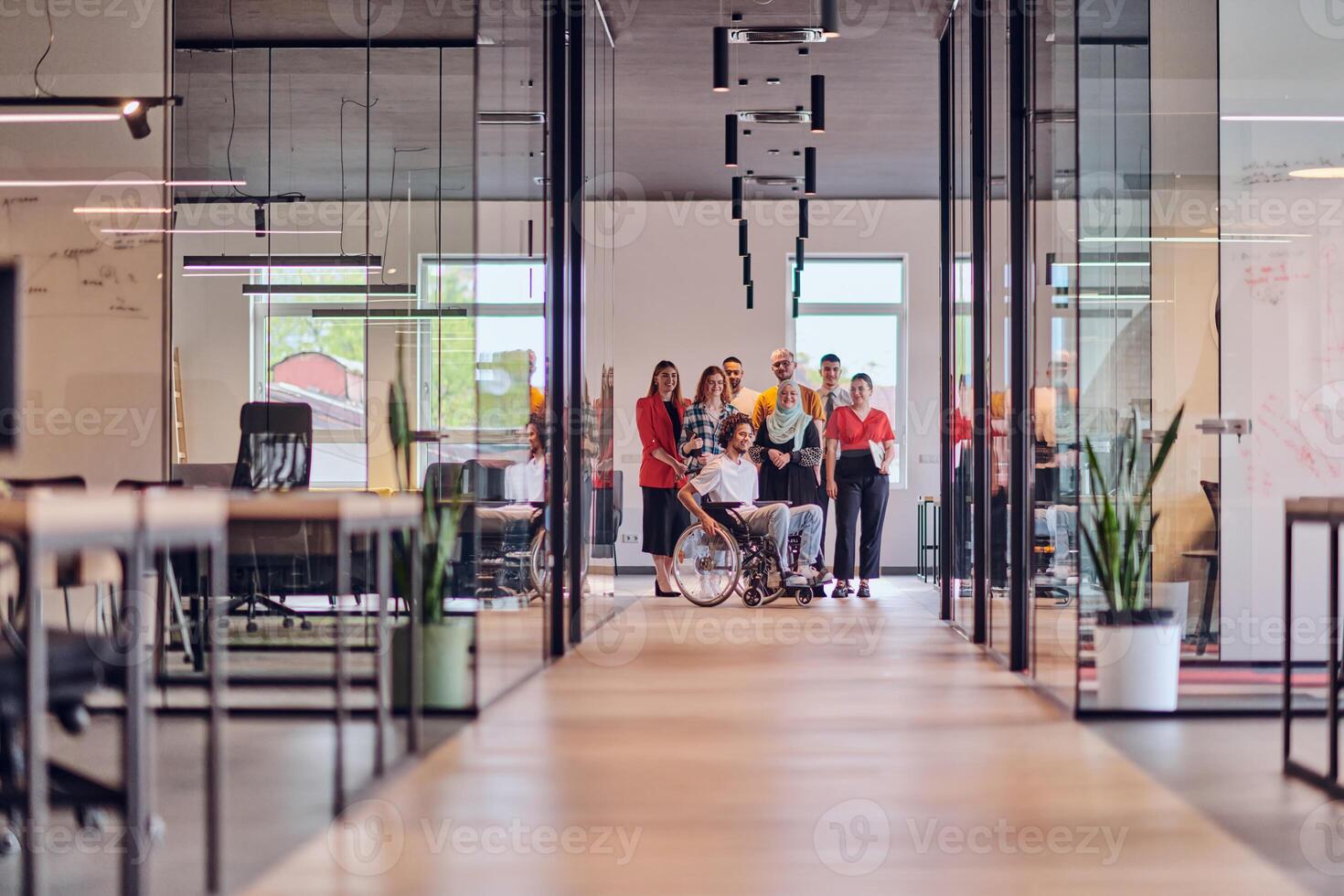 A diverse group of young business people congregates within a modern startup's glass-enclosed office, featuring inclusivity with a person in a wheelchair, an African American young man , and a hijab photo