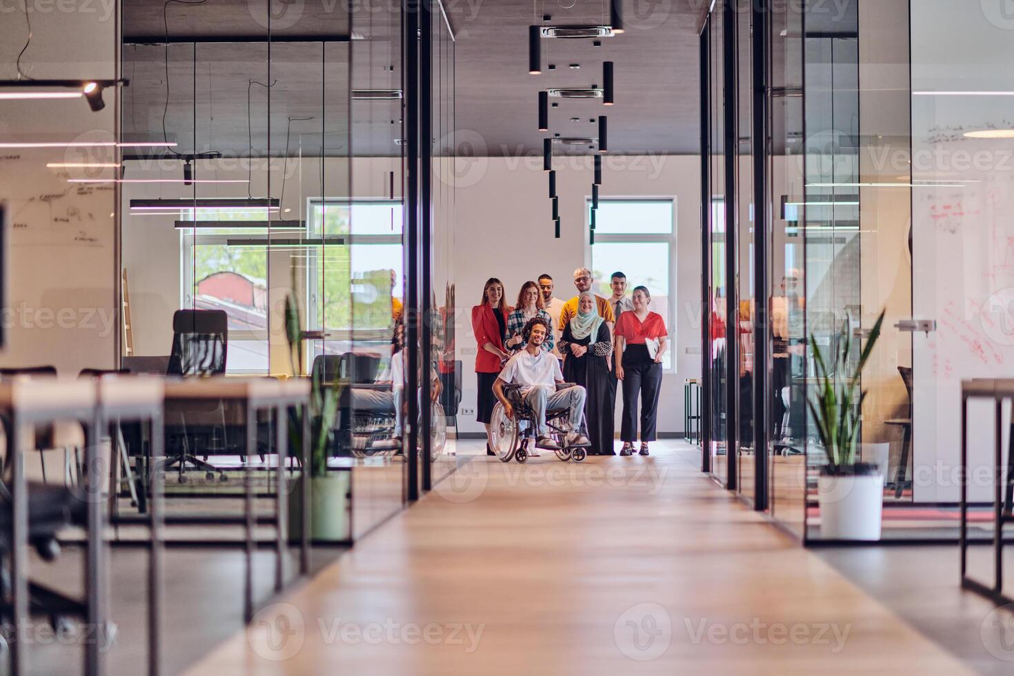 A diverse group of young business people congregates within a modern startup's glass-enclosed office, featuring inclusivity with a person in a wheelchair, an African American young man , and a hijab photo