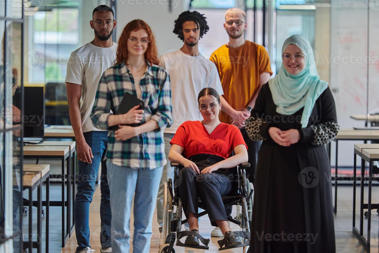 A diverse group of young business people congregates within a modern startup's glass-enclosed office, featuring inclusivity with a person in a wheelchair, an African American young man , and a hijab photo