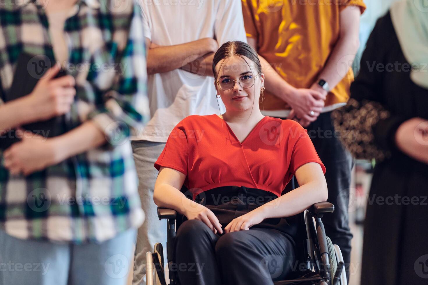 A diverse group of business people walking a corridor in the glass-enclosed office of a modern startup, including a person in a wheelchair and a woman wearing a hijab, showing a dynamic mix of photo