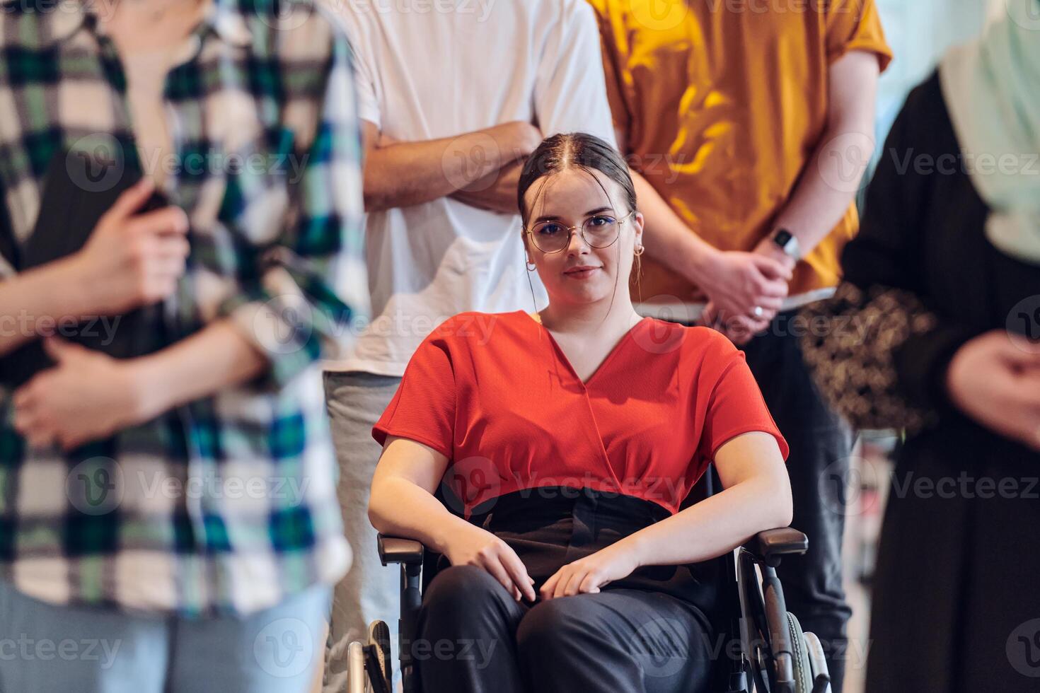 A diverse group of business people walking a corridor in the glass-enclosed office of a modern startup, including a person in a wheelchair and a woman wearing a hijab, showing a dynamic mix of photo