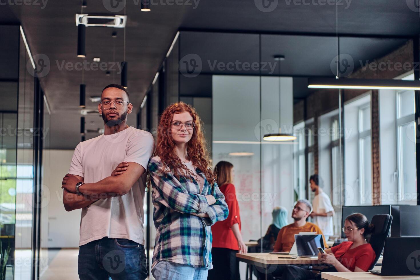 A young African American businessman and a modern businesswoman with orange hair stand side by side, arms crossed, exuding confidence and unity in a contemporary office setting, epitomizing dynamic photo
