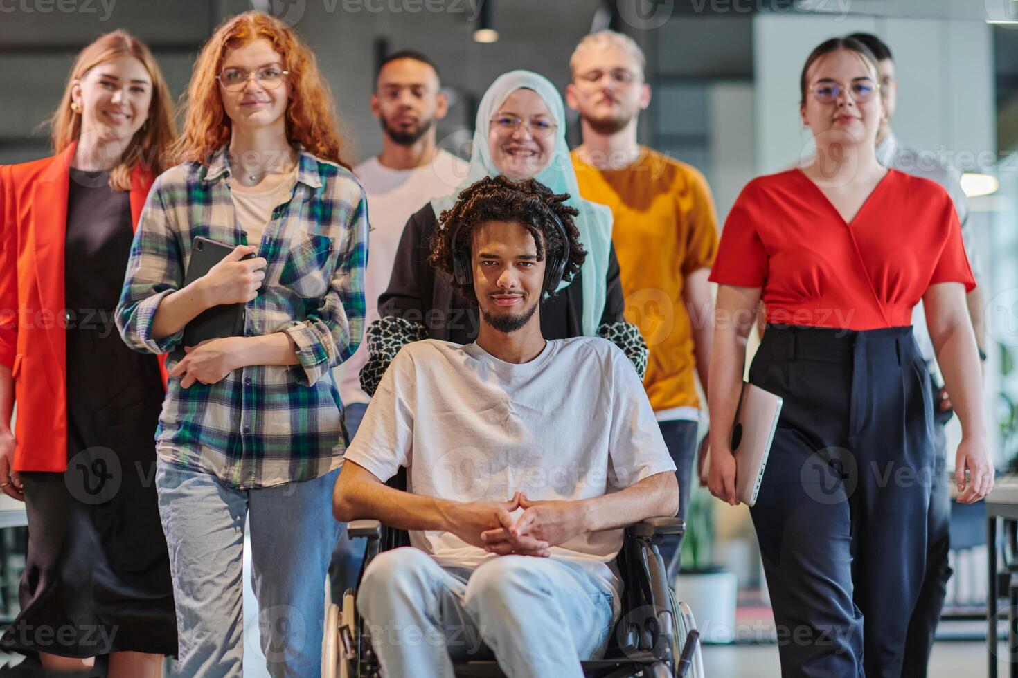 A diverse group of young business people congregates within a modern startup's glass-enclosed office, featuring inclusivity with a person in a wheelchair, an African American young man , and a hijab photo