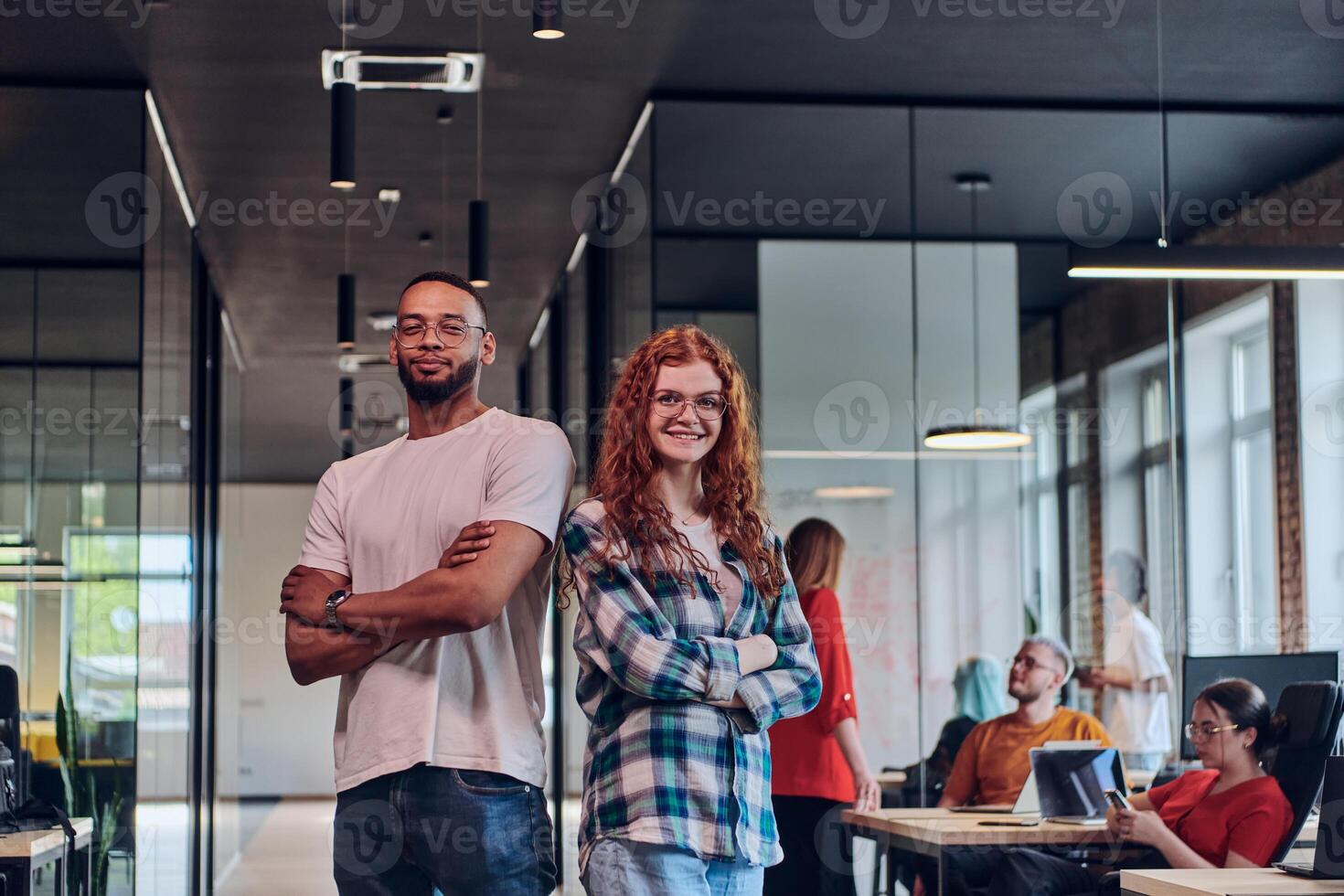 A young African American businessman and a modern businesswoman with orange hair stand side by side, arms crossed, exuding confidence and unity in a contemporary office setting, epitomizing dynamic photo