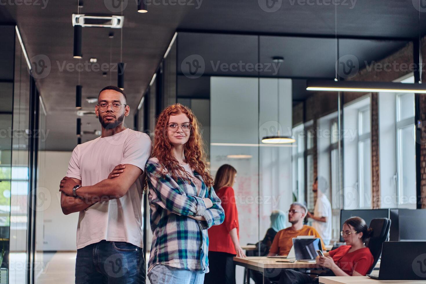 A young African American businessman and a modern businesswoman with orange hair stand side by side, arms crossed, exuding confidence and unity in a contemporary office setting, epitomizing dynamic photo