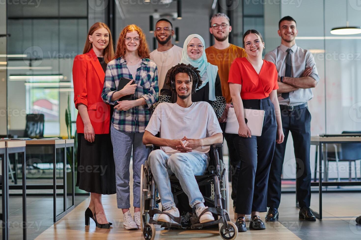 A diverse group of young business people congregates within a modern startup's glass-enclosed office, featuring inclusivity with a person in a wheelchair, an African American young man , and a hijab photo