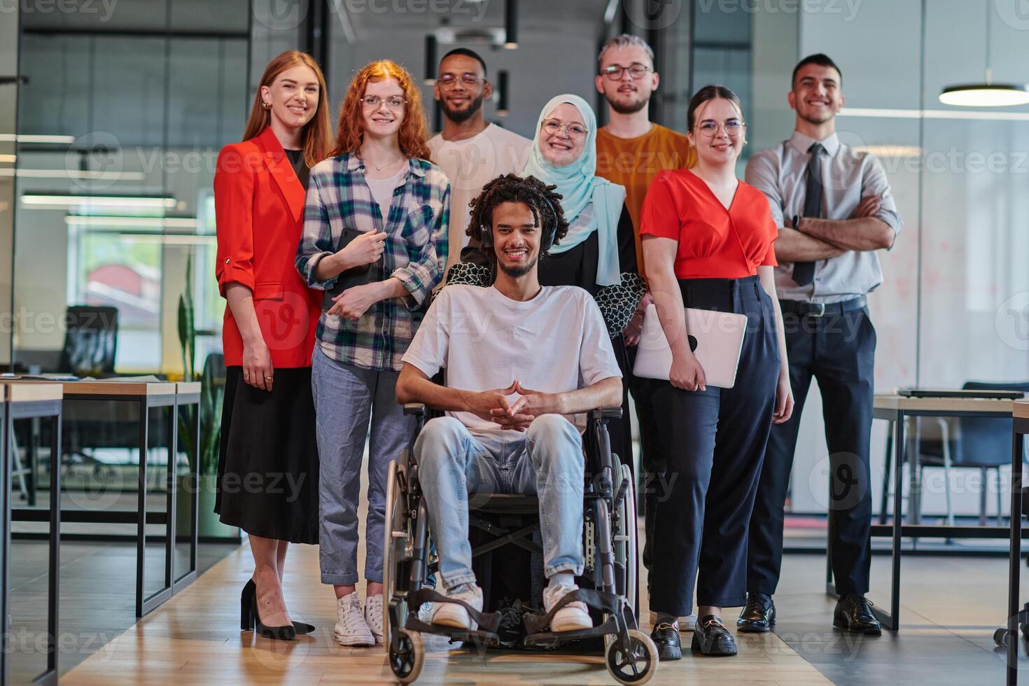 A diverse group of young business people congregates within a modern startup's glass-enclosed office, featuring inclusivity with a person in a wheelchair, an African American young man , and a hijab photo
