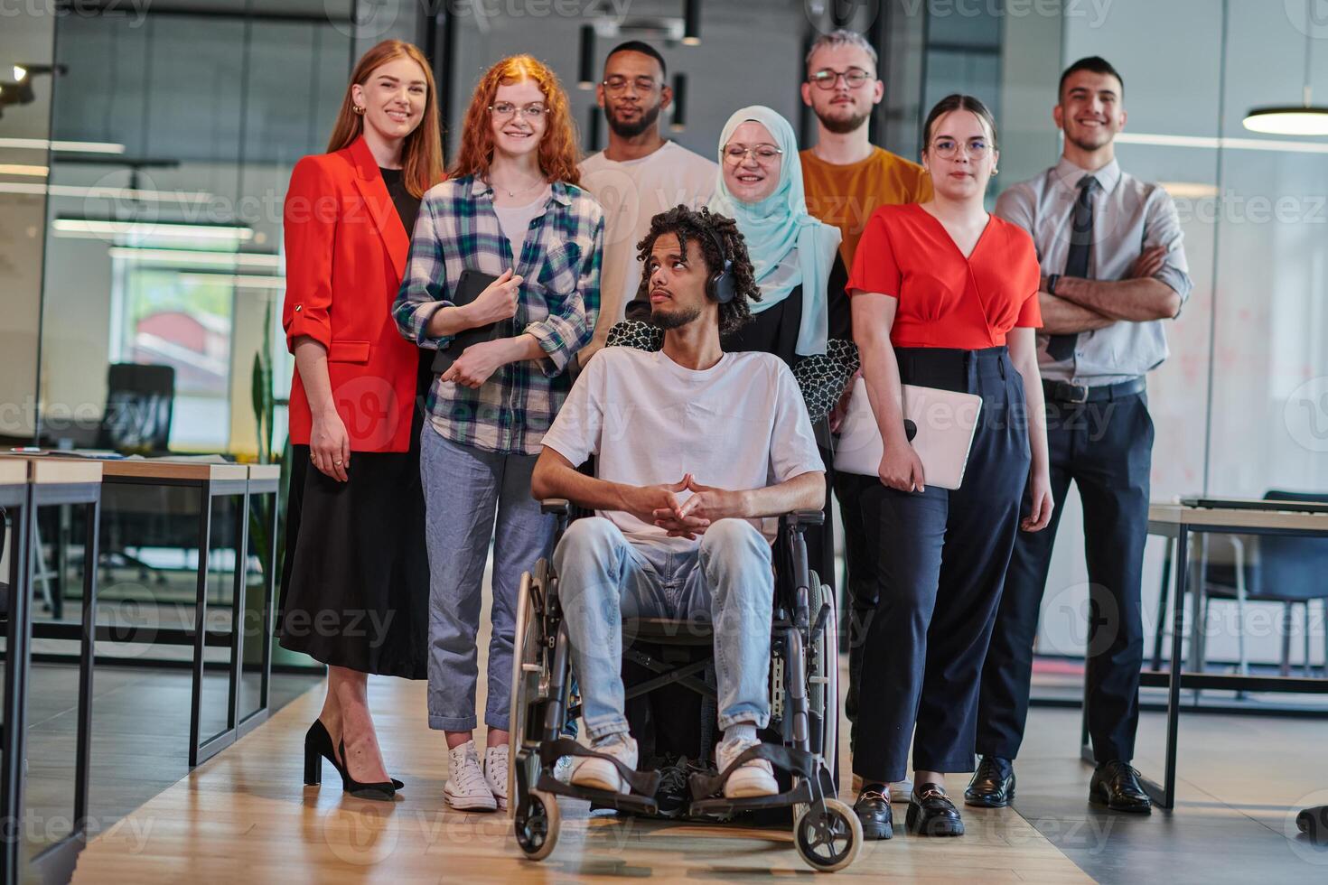 A diverse group of young business people congregates within a modern startup's glass-enclosed office, featuring inclusivity with a person in a wheelchair, an African American young man , and a hijab photo