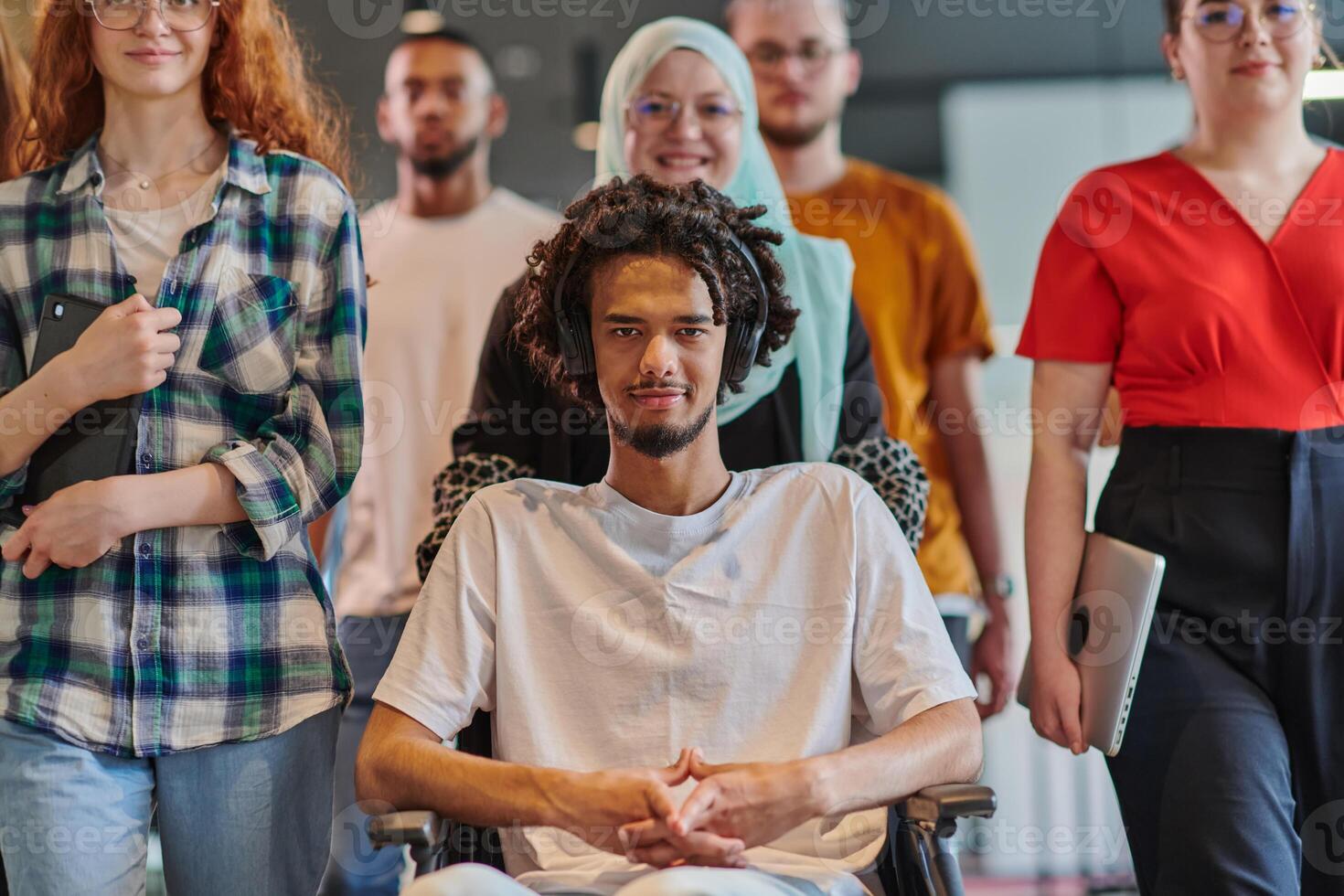 A diverse group of young business people congregates within a modern startup's glass-enclosed office, featuring inclusivity with a person in a wheelchair, an African American young man , and a hijab photo