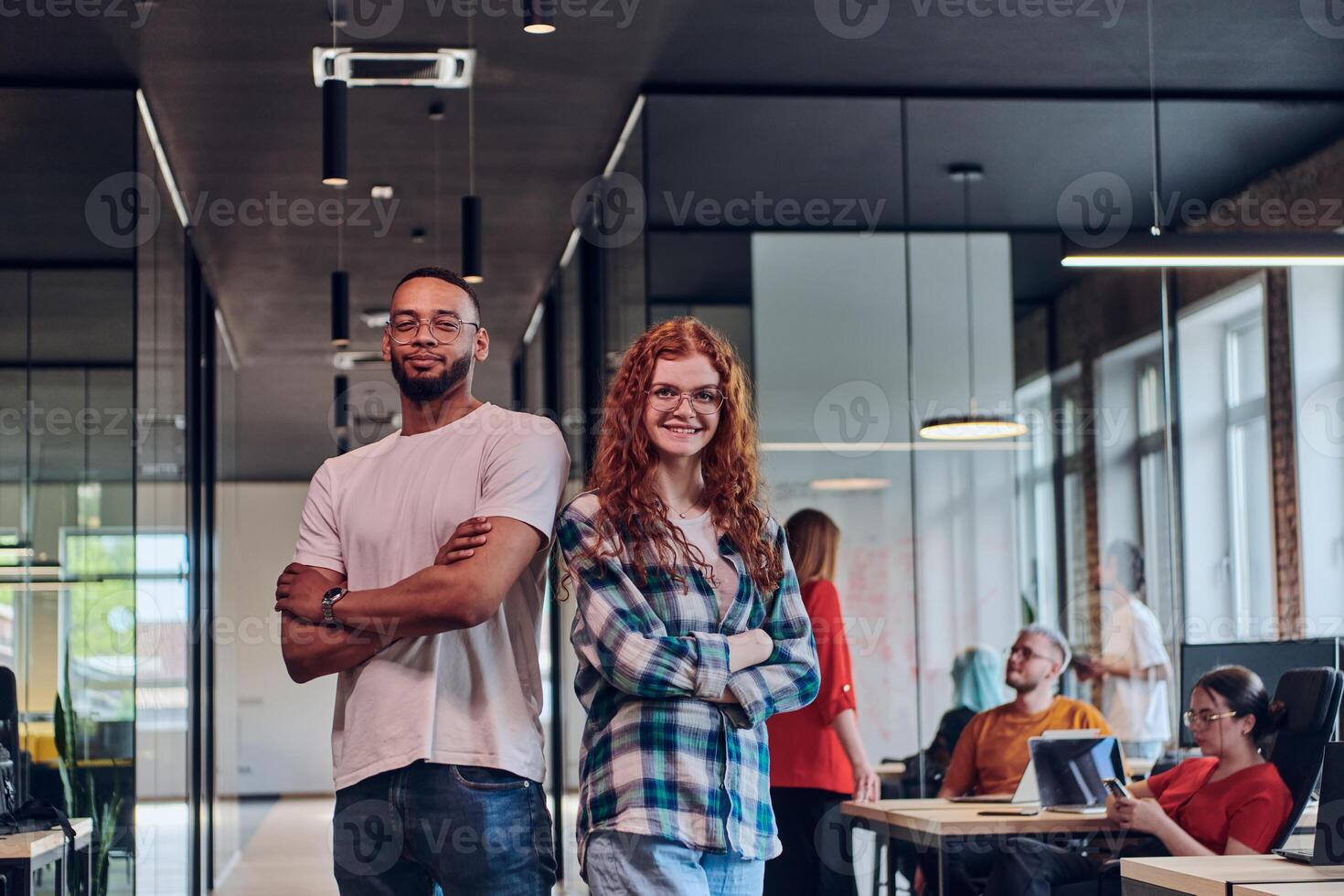A young African American businessman and a modern businesswoman with orange hair stand side by side, arms crossed, exuding confidence and unity in a contemporary office setting, epitomizing dynamic photo