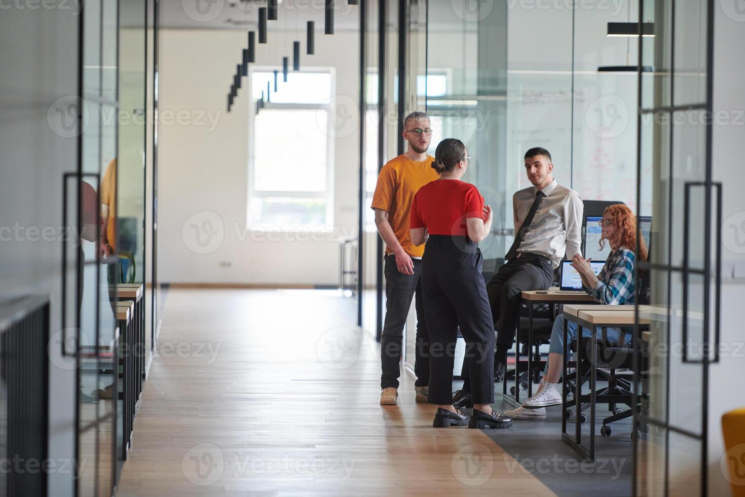 A business group, including an African American businessman in a wheelchair, collaborates within a modern glass office, actively engaged around a computer and laptop, collectively solving diverse photo