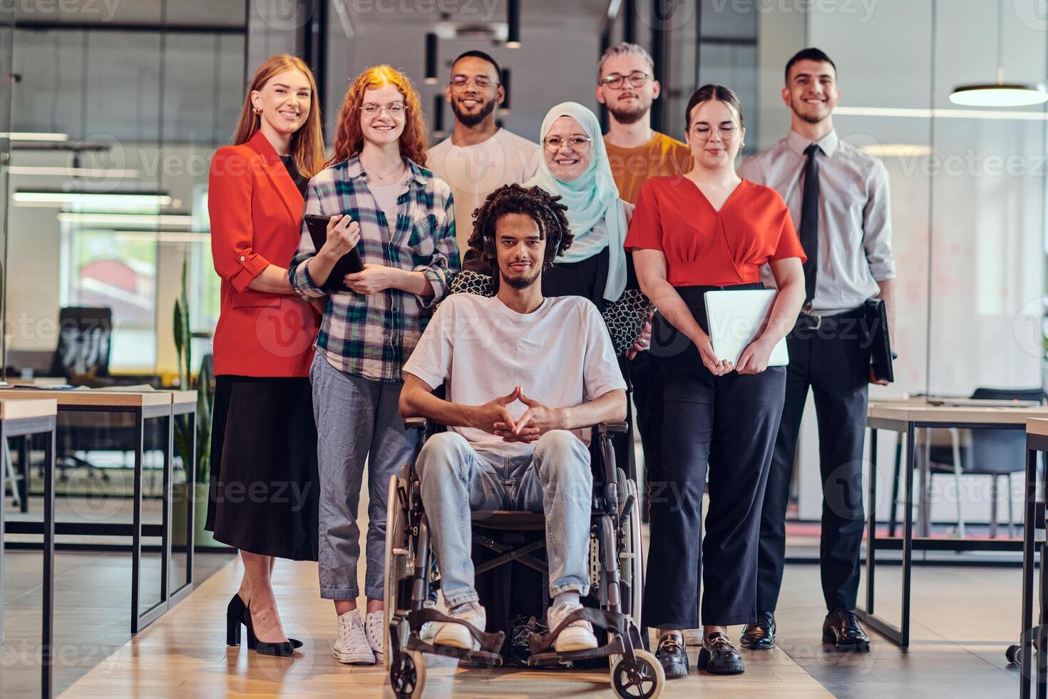 A diverse group of young business people congregates within a modern startup's glass-enclosed office, featuring inclusivity with a person in a wheelchair, an African American young man , and a hijab photo