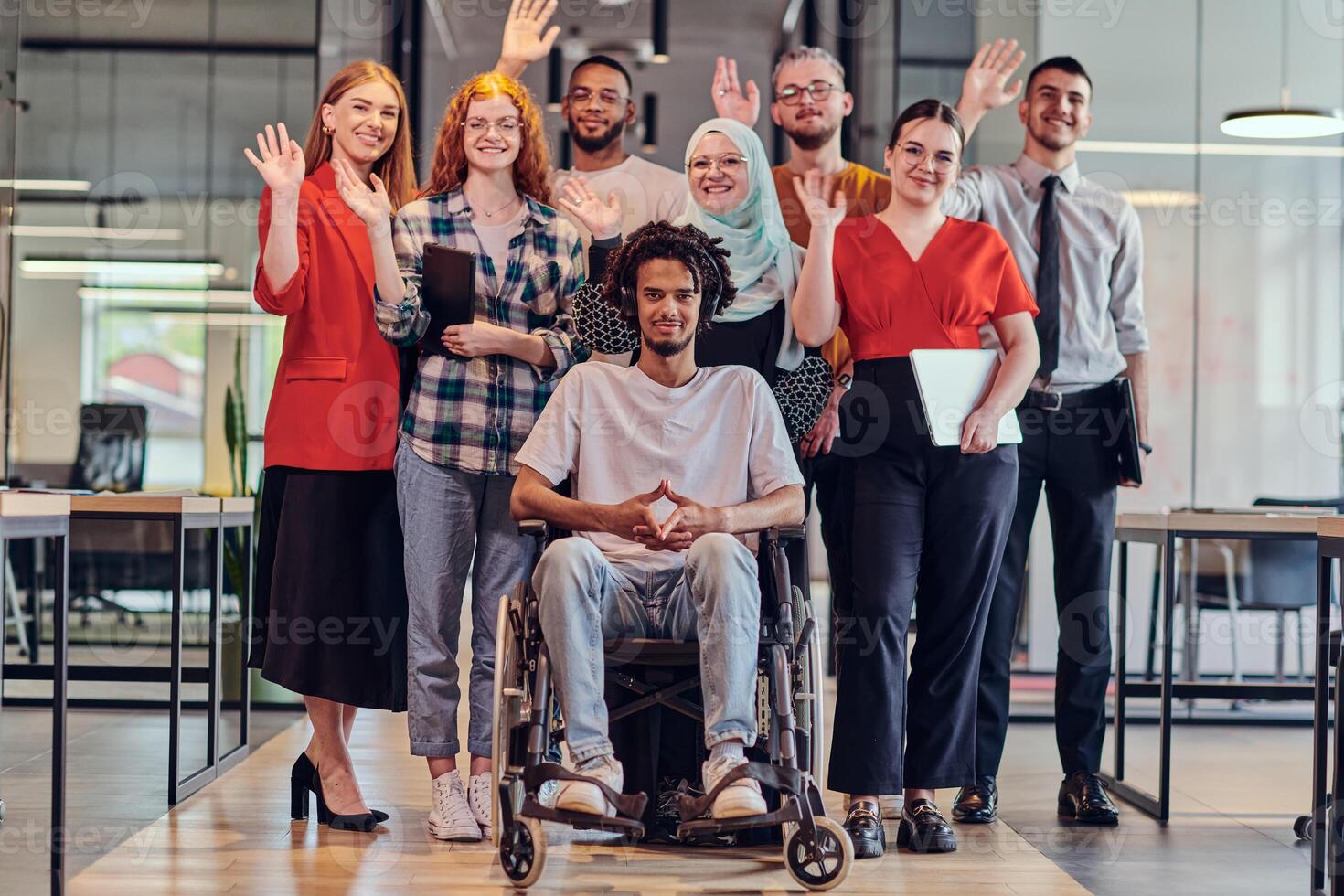 A diverse group of young business people congregates within a modern startup's glass-enclosed office, featuring inclusivity with a person in a wheelchair, an African American young man , and a hijab photo