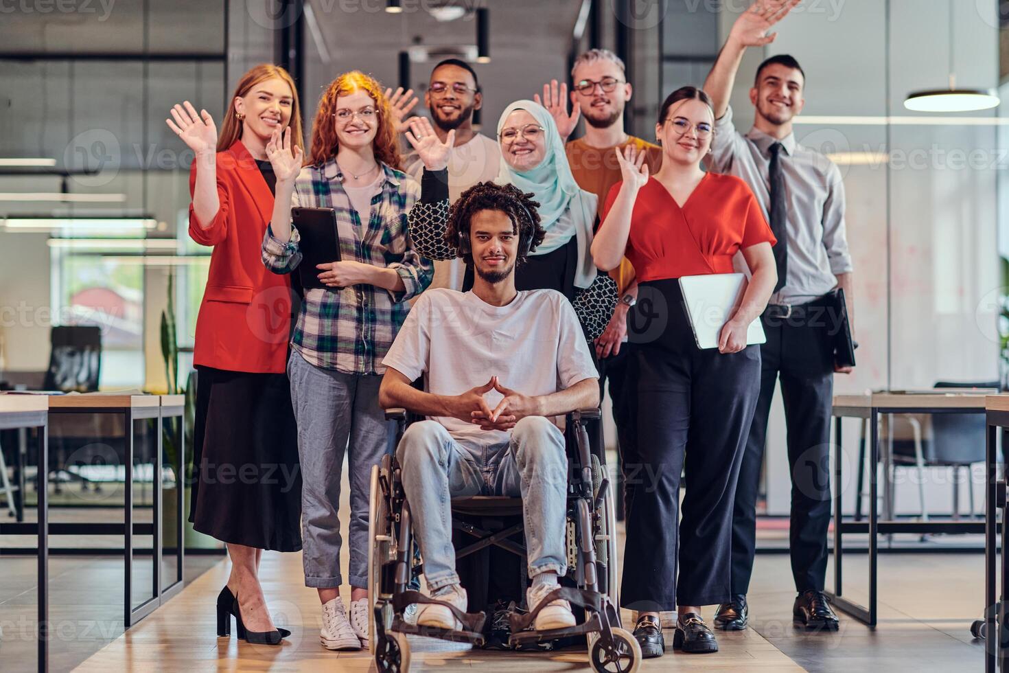 A diverse group of young business people congregates within a modern startup's glass-enclosed office, featuring inclusivity with a person in a wheelchair, an African American young man , and a hijab photo
