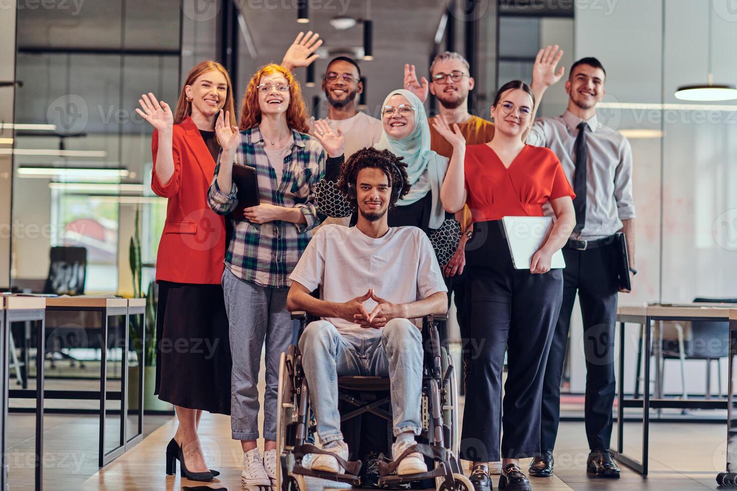A diverse group of young business people congregates within a modern startup's glass-enclosed office, featuring inclusivity with a person in a wheelchair, an African American young man , and a hijab photo