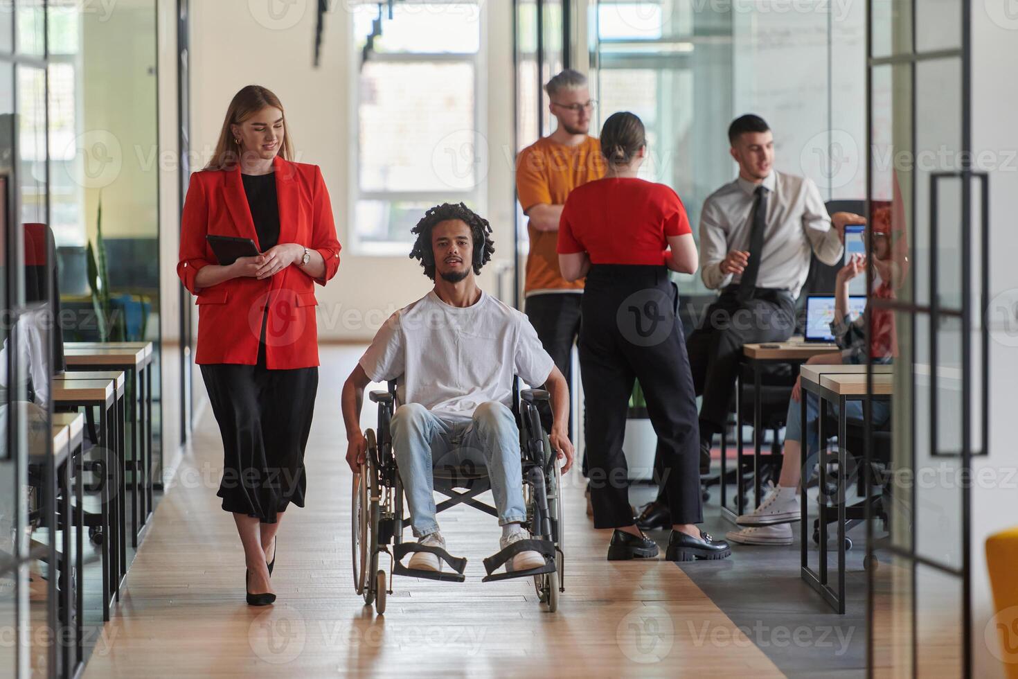 A group of young business people in a modern glass-walled office captures the essence of diversity and collaboration, while two colleagues, including an African American businessman in a wheelchair photo
