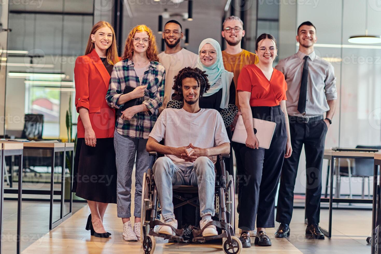 A diverse group of young business people congregates within a modern startup's glass-enclosed office, featuring inclusivity with a person in a wheelchair, an African American young man , and a hijab photo