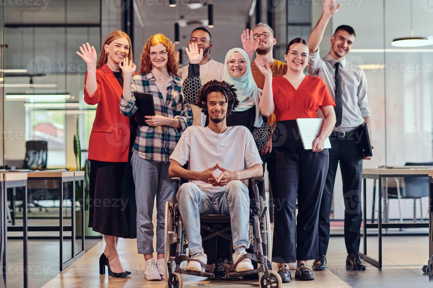 A diverse group of young business people congregates within a modern startup's glass-enclosed office, featuring inclusivity with a person in a wheelchair, an African American young man , and a hijab photo